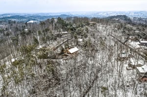 Aerial winter view of the property nestled among snowcovered trees in a peaceful forested neighborhood.