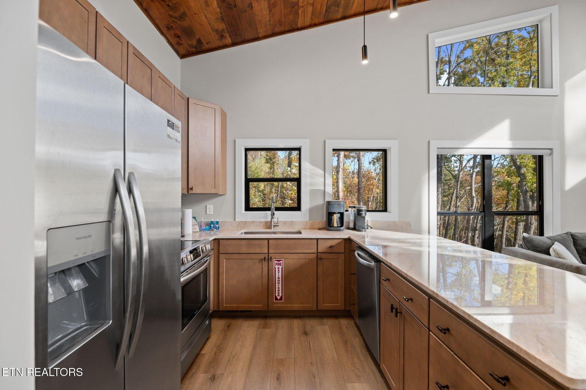Step into a bright, modern kitchen where natural light pours through large windows framing fall foliage. Sleek countertops and warm wood tones create a welcoming space for your morning coffee or prepa