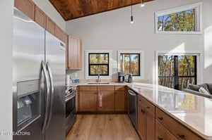 Step into a bright, modern kitchen where natural light pours through large windows framing fall foliage. Sleek countertops and warm wood tones create a welcoming space for your morning coffee or prepa