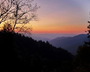 Breathtaking mountain sunset paints the sky in warm hues over rolling forested peaks and valleys.