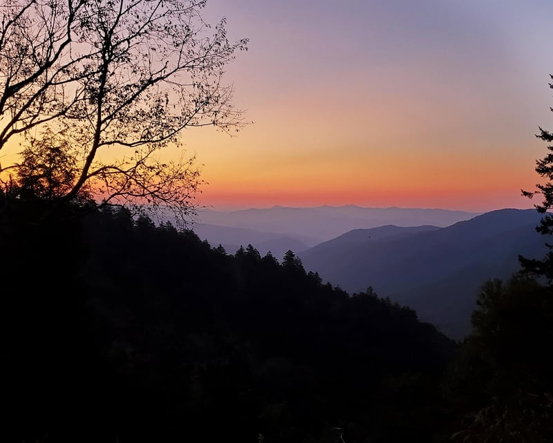 Breathtaking mountain sunset paints the sky in warm hues over rolling forested peaks and valleys.