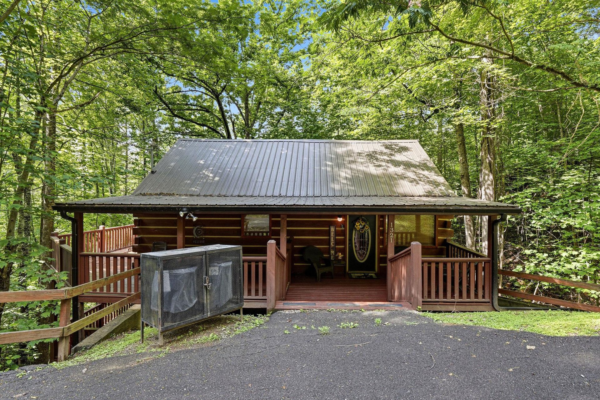 A charming log cabin nestled in lush greenery with a covered porch and convenient parking, offering a peaceful woodland retreat surrounded by towering trees and natural beauty.