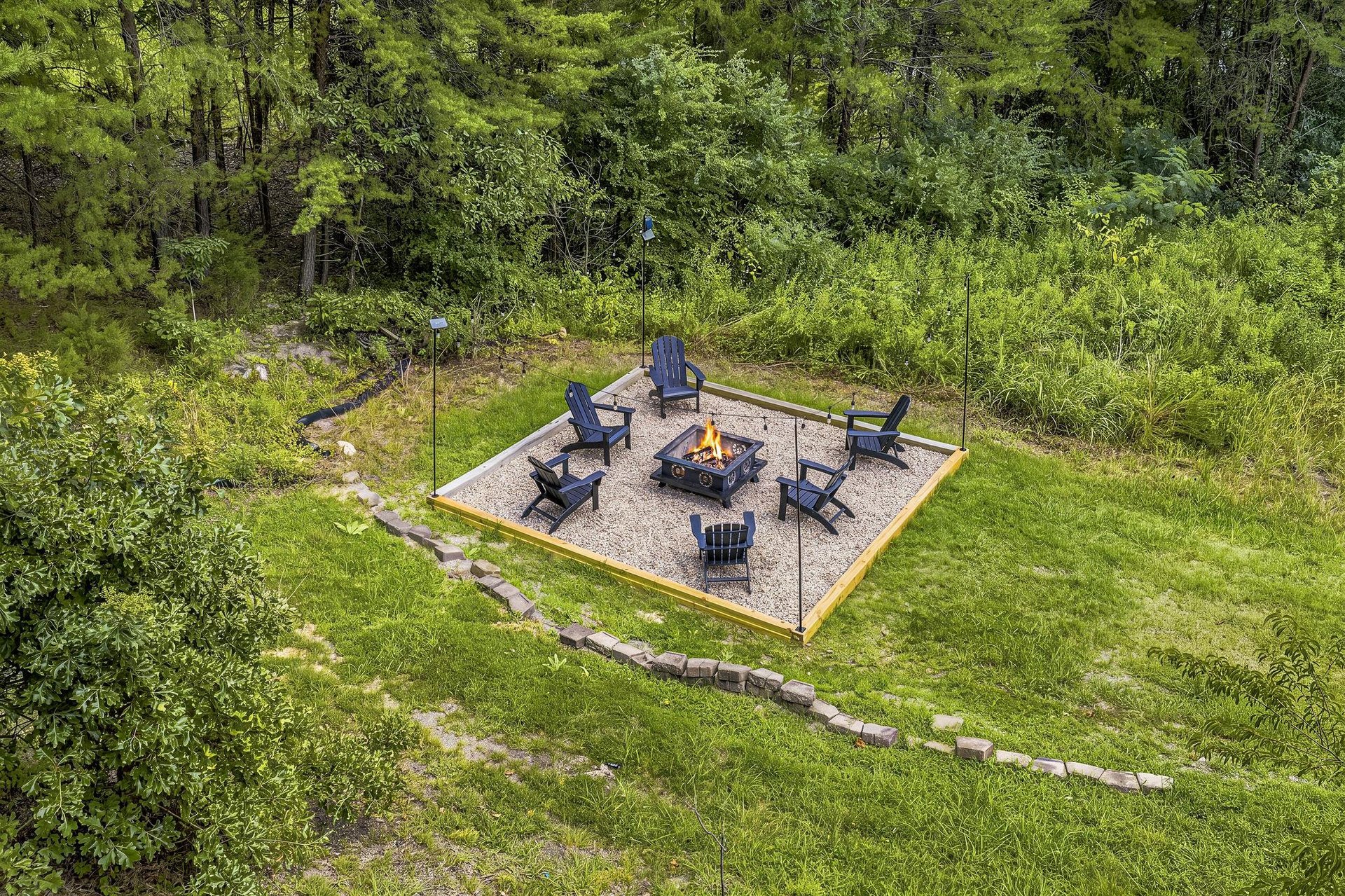 Aerial view of the propertys fire pit area, nestled in a wooded landscape with surrounding trails and lush greenery.