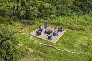 Aerial view of the propertys fire pit area, nestled in a wooded landscape with surrounding trails and lush greenery.