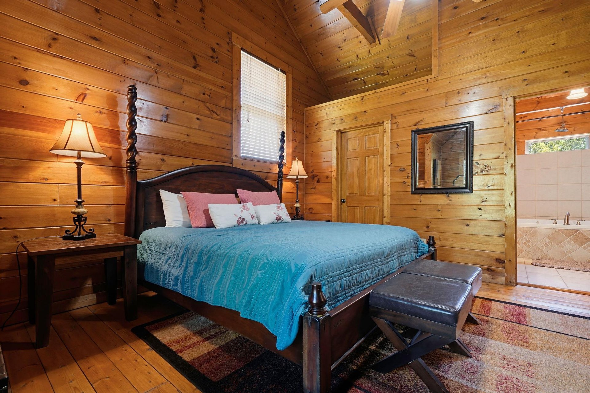 Your cozy cabin bedroom awaits with rustic woodpaneled walls, vaulted ceilings, and a soft bed dressed in turquoise. Warm lamplight and charming touches create the perfect mountain retreat.