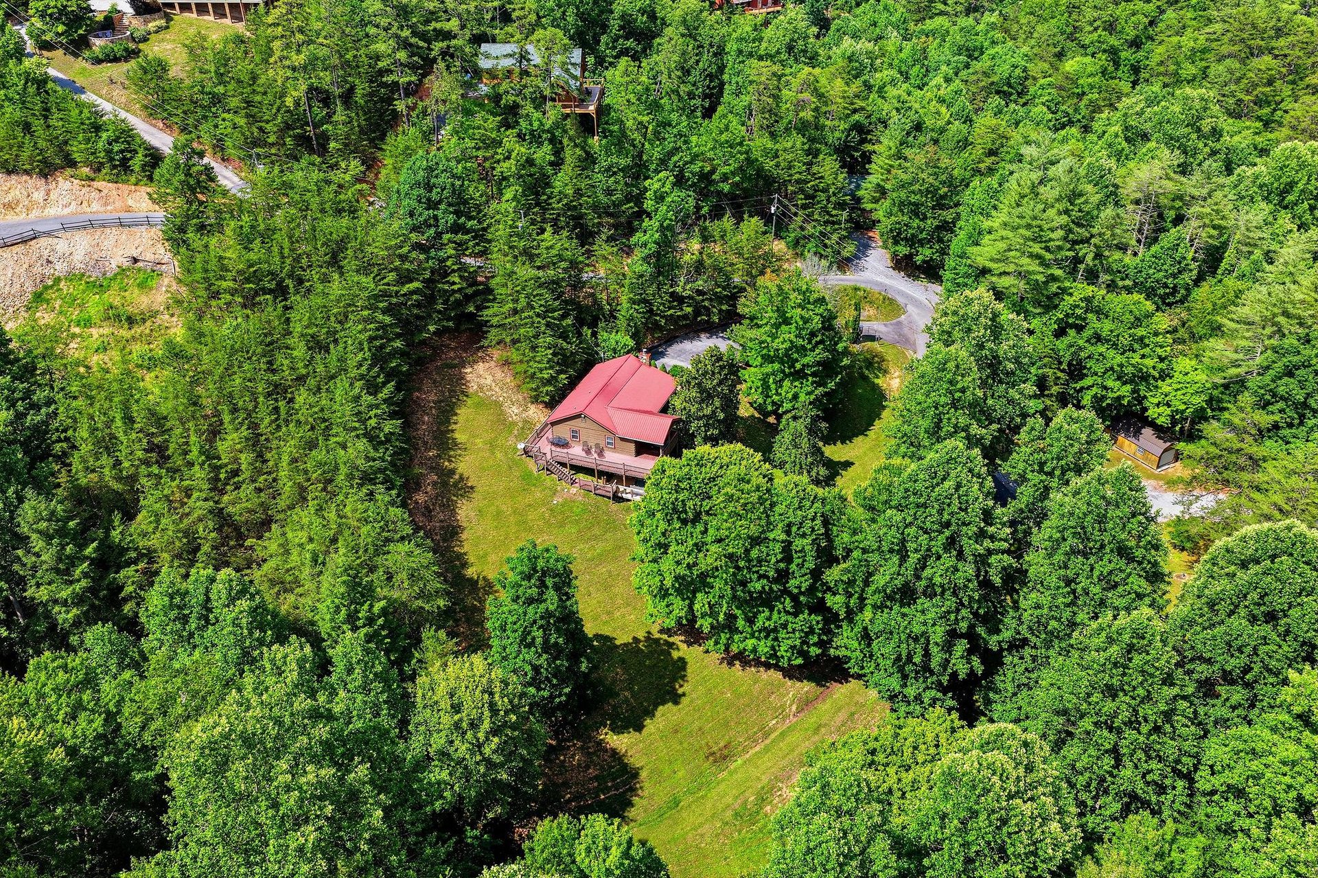 This secluded mountain cabin with its distinctive red roof sits nestled within dense forest, offering a private wooded retreat away from everyday life.