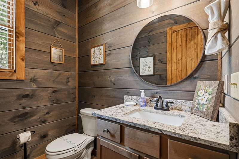 Step into your rusticchic bathroom with warm wood paneling, a sleek granite vanity, and charming botanical accents that create a cozy, natureinspired retreat.
