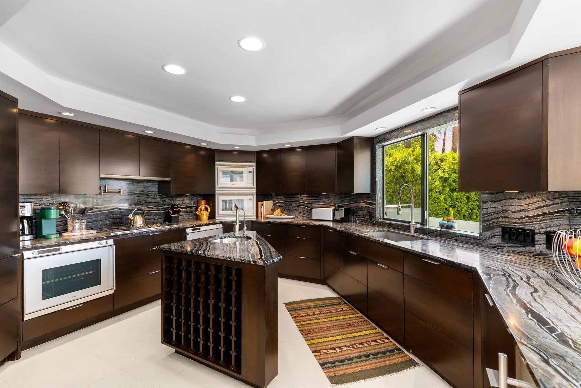 Stainless steel appliances, cooking essentials, island with wine storage, and pool views.