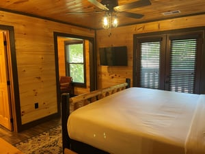 Unwind in your rustic cabin bedroom, where warm wood tones and a cozy ceiling fan create the perfect retreat after exploring the outdoors.