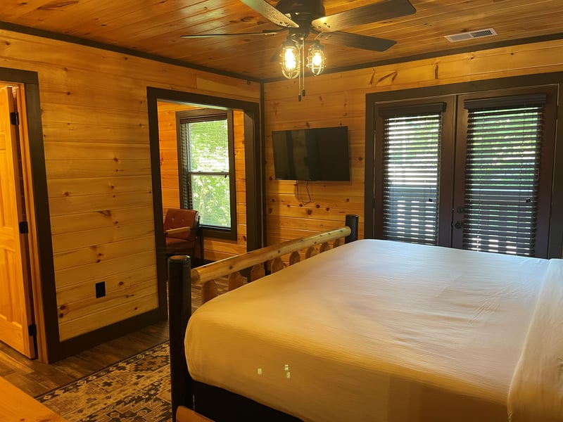 Unwind in your rustic cabin bedroom, where warm wood tones and a cozy ceiling fan create the perfect retreat after exploring the outdoors.