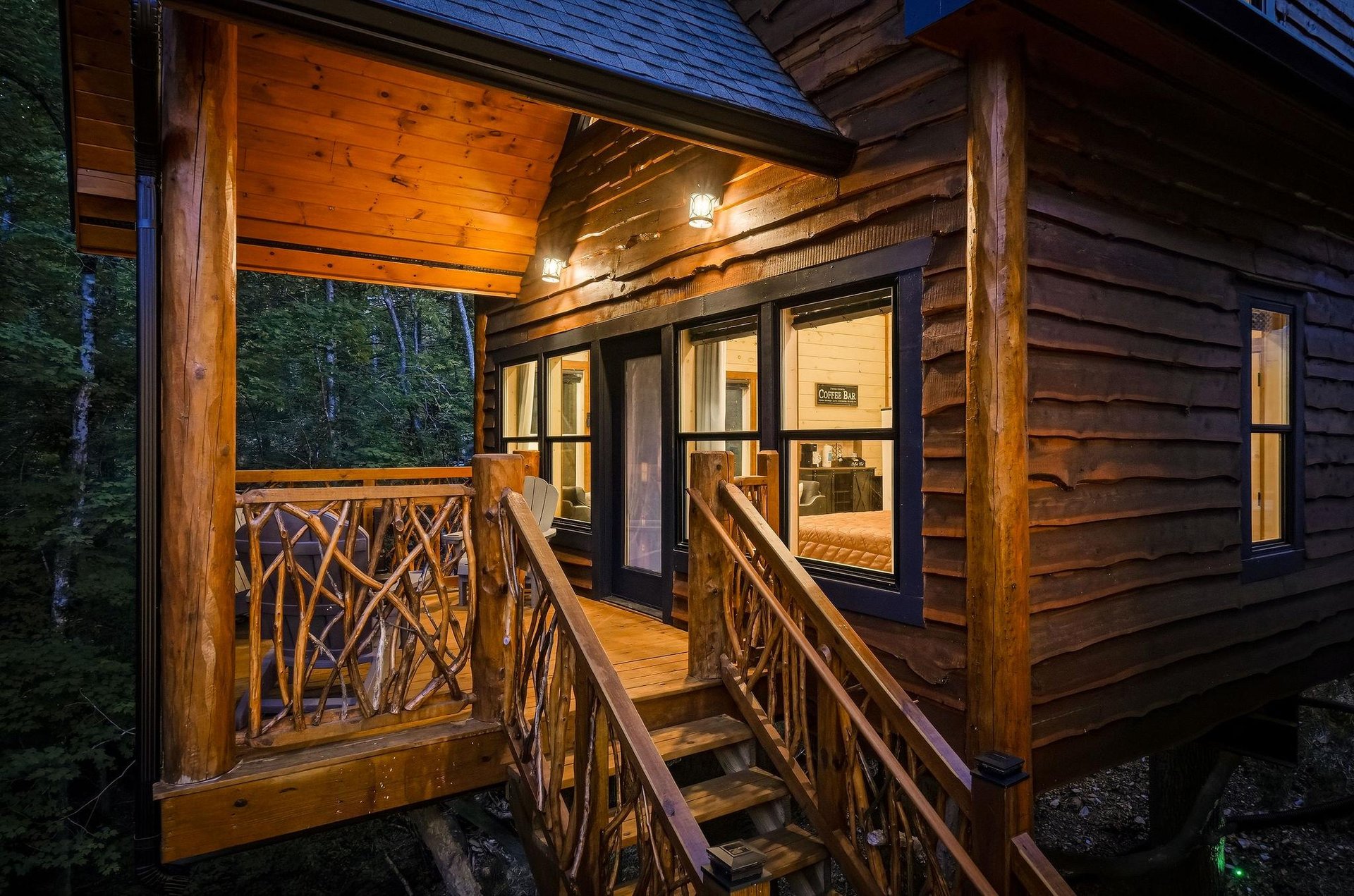 This rustic cabin entrance invites you to step onto your private covered balcony, where warm wood tones and handcrafted railings frame the natural forest beyond.