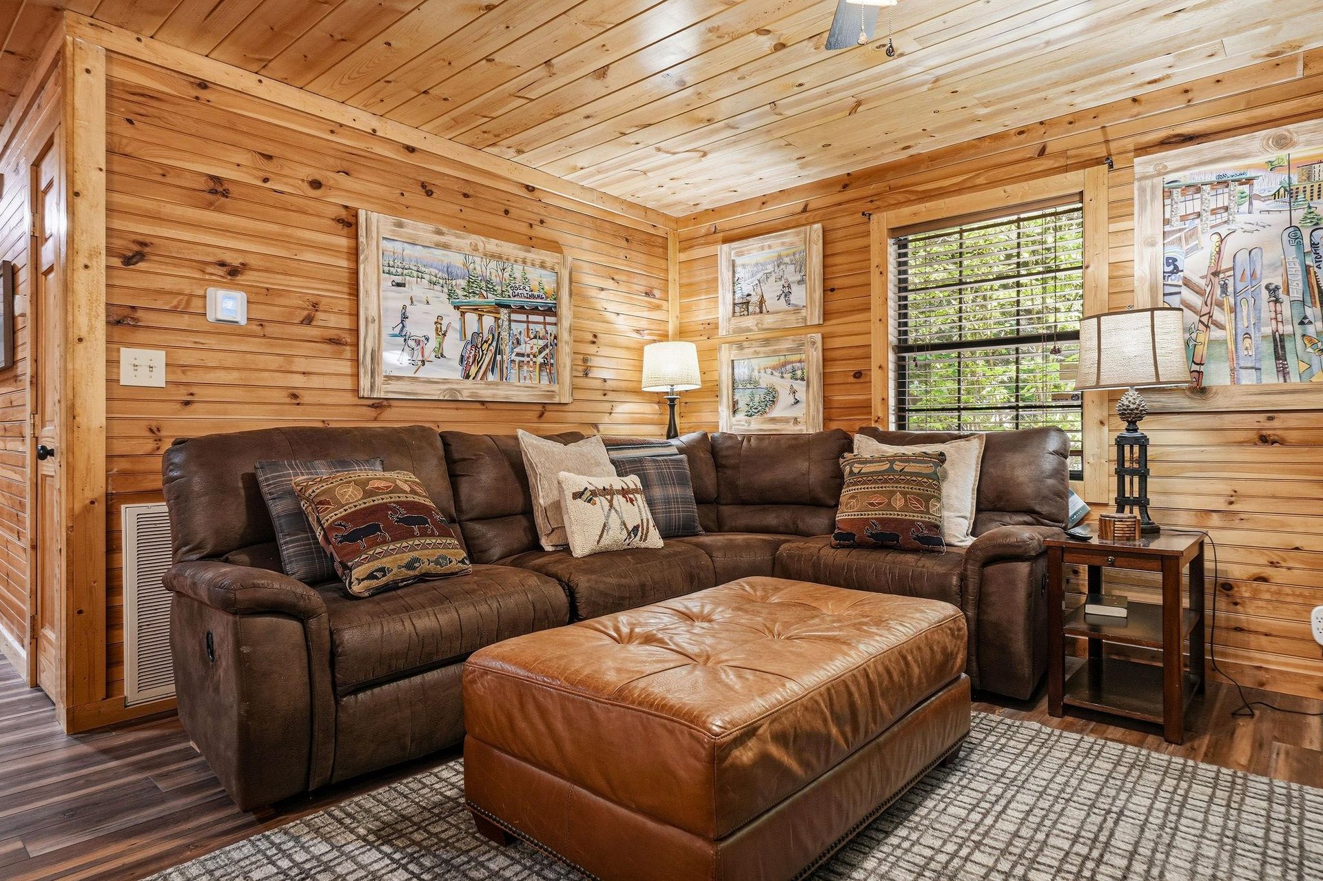 Step into your cozy cabin retreat with warm woodpaneled walls and a plush leather sectional sofa, perfect for unwinding after a day of mountain adventures.