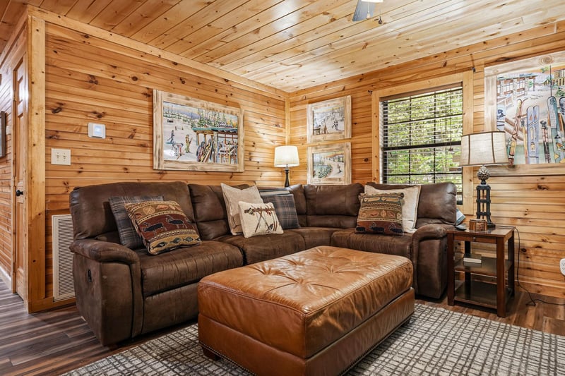 Step into your cozy cabin retreat with warm woodpaneled walls and a plush leather sectional sofa, perfect for unwinding after a day of mountain adventures.