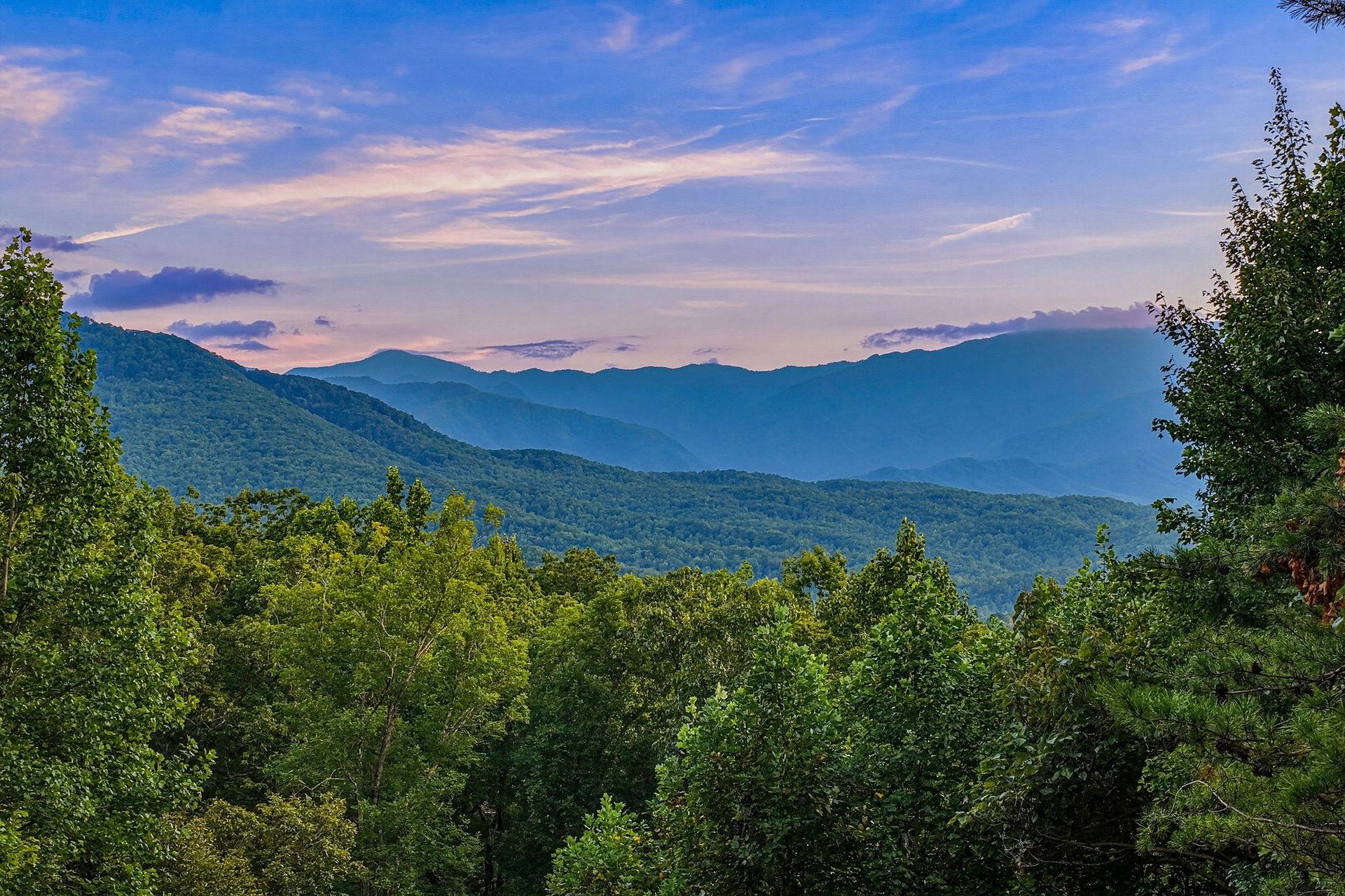 Majestic mountain ranges frame the property, with layers of forested peaks stretching toward a serene twilight sky—a stunning natural backdrop to your mountain escape.