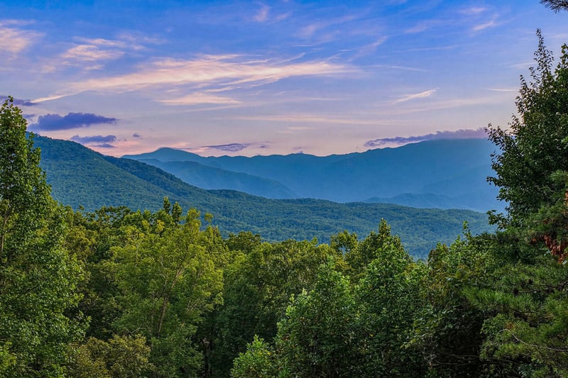 Majestic mountain ranges frame the property, with layers of forested peaks stretching toward a serene twilight sky—a stunning natural backdrop to your mountain escape.