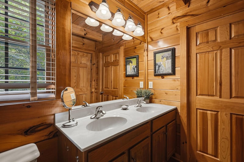 Step into your rustic bathroom where warm wood surrounds you and natural light filters through wooden blinds, creating a cozy mountain retreat atmosphere.