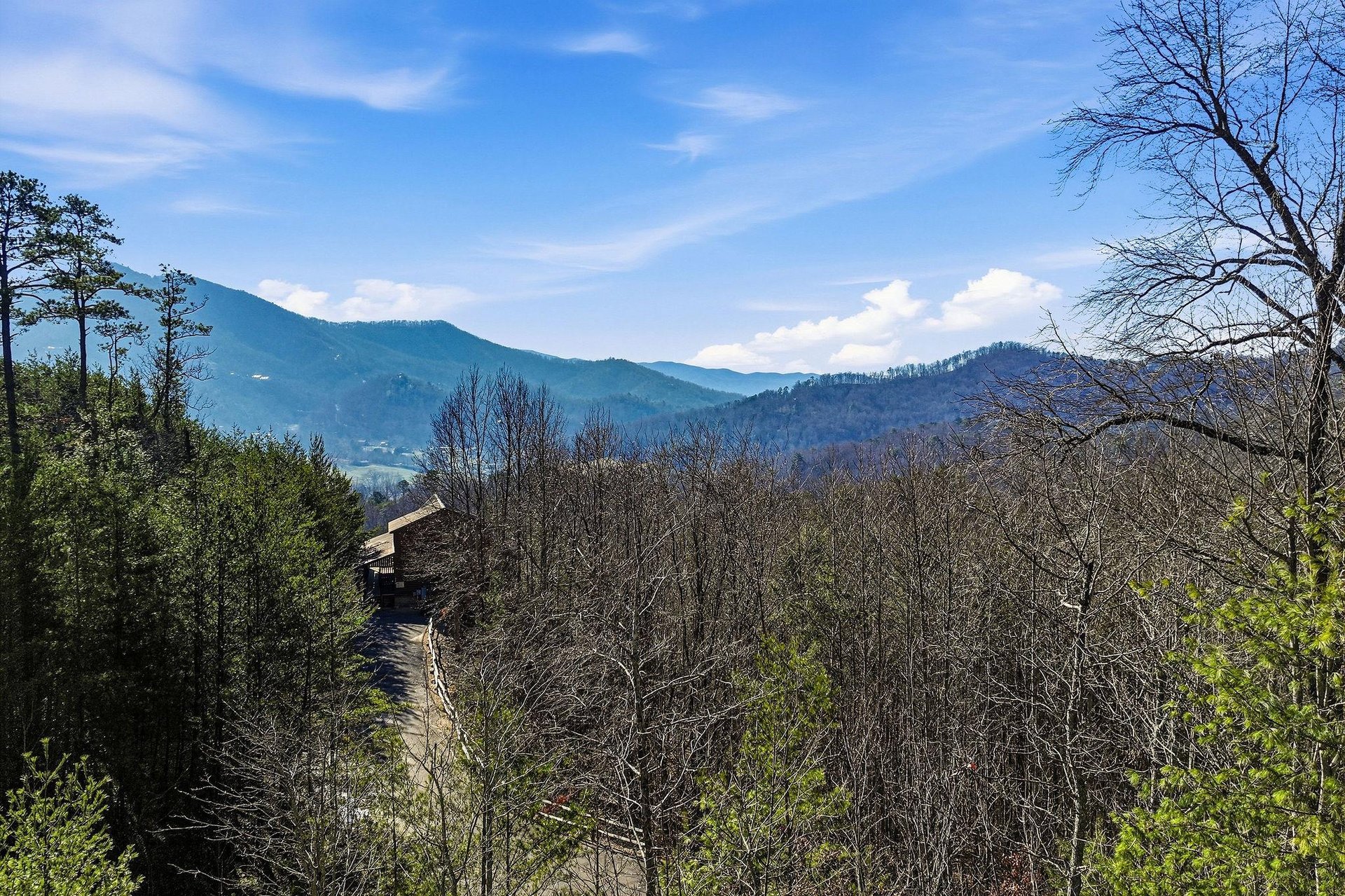 Panoramic mountain views stretch across rolling forested hills beneath a bright blue sky dotted with white clouds.