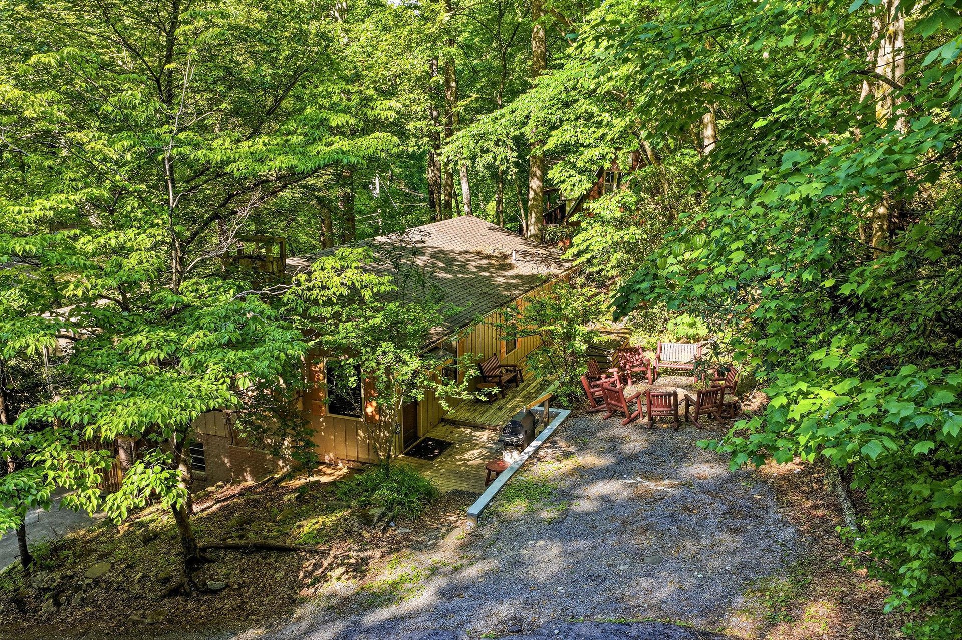 The property sits peacefully in a lush forest setting, offering a serene retreat surrounded by nature, with ample parking and outdoor seating areas.