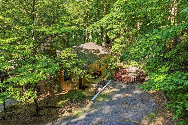 The property sits peacefully in a lush forest setting, offering a serene retreat surrounded by nature, with ample parking and outdoor seating areas.