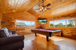 Challenge your friends to a game in this rustic billiard room with warm wood paneling, cozy seating, and stunning mountain views through expansive windows.