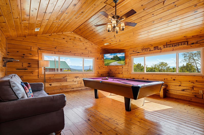 Challenge your friends to a game in this rustic billiard room with warm wood paneling, cozy seating, and stunning mountain views through expansive windows.