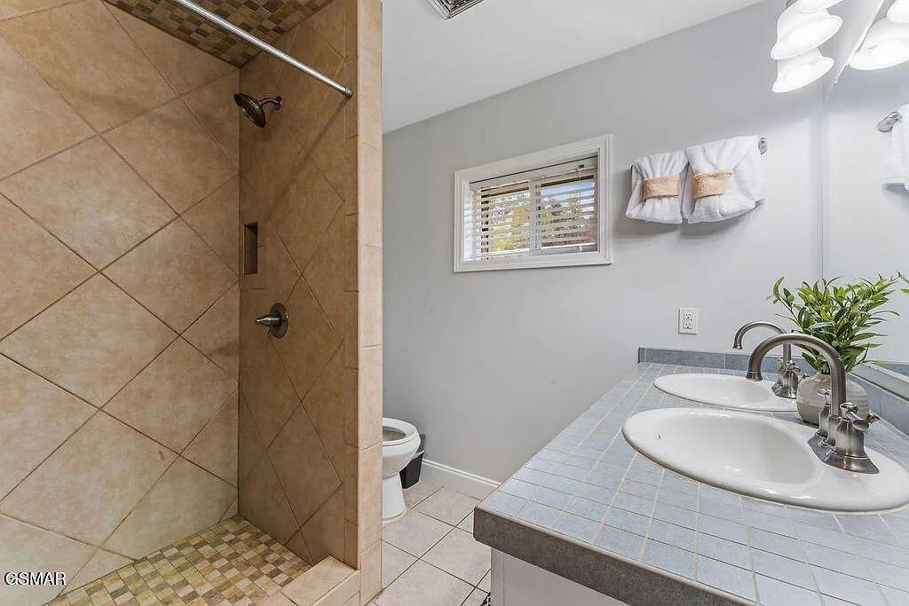 Refresh in your private bathroom featuring a spacious tiled shower, dual sinks, and thoughtful touches like fresh towels and greenery.