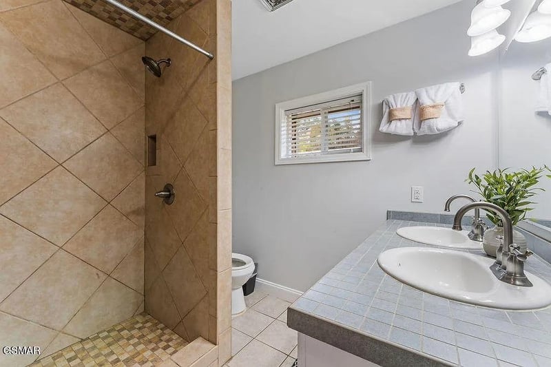 Refresh in your private bathroom featuring a spacious tiled shower, dual sinks, and thoughtful touches like fresh towels and greenery.