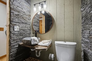 Step into your stylish powder room featuring a stunning stone vessel sink, elegant round mirror, and dramatic textured accent walls that create a spalike retreat.