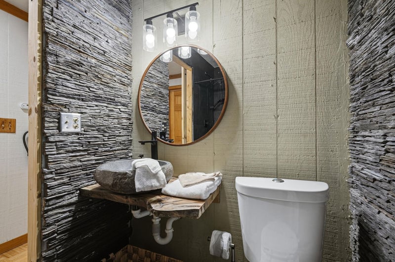 Step into your stylish powder room featuring a stunning stone vessel sink, elegant round mirror, and dramatic textured accent walls that create a spalike retreat.
