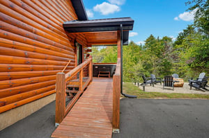 The property features a charming log cabin exterior surrounded by lush greenery, with a private deck and hot tub for your relaxation. Unwind in the fire pit seating area under open skies.