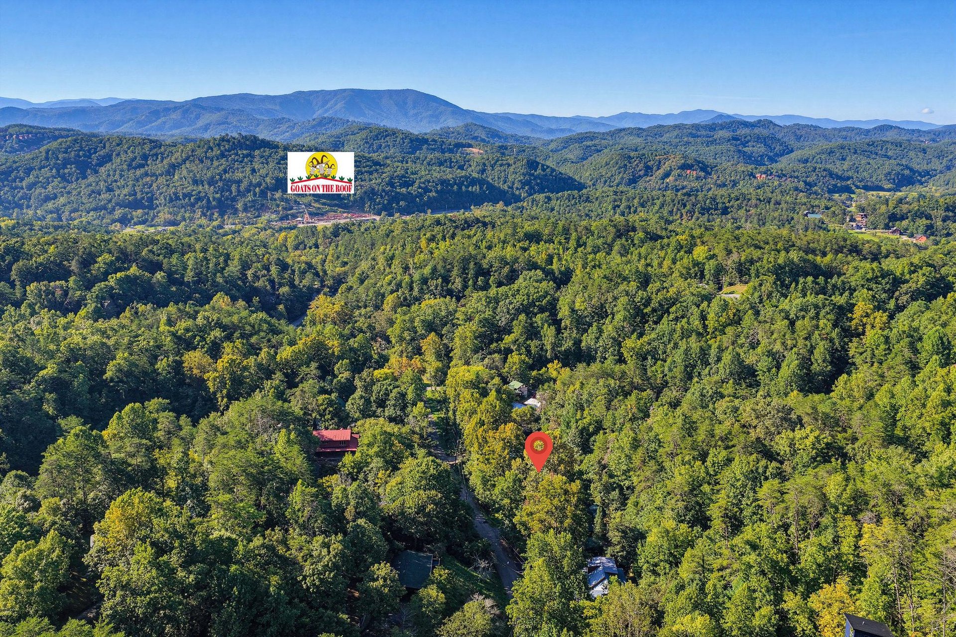 Aerial view of forested hills surrounding the property, with mountain ranges visible in the distance. The location sign identifies the property within the natural landscape.