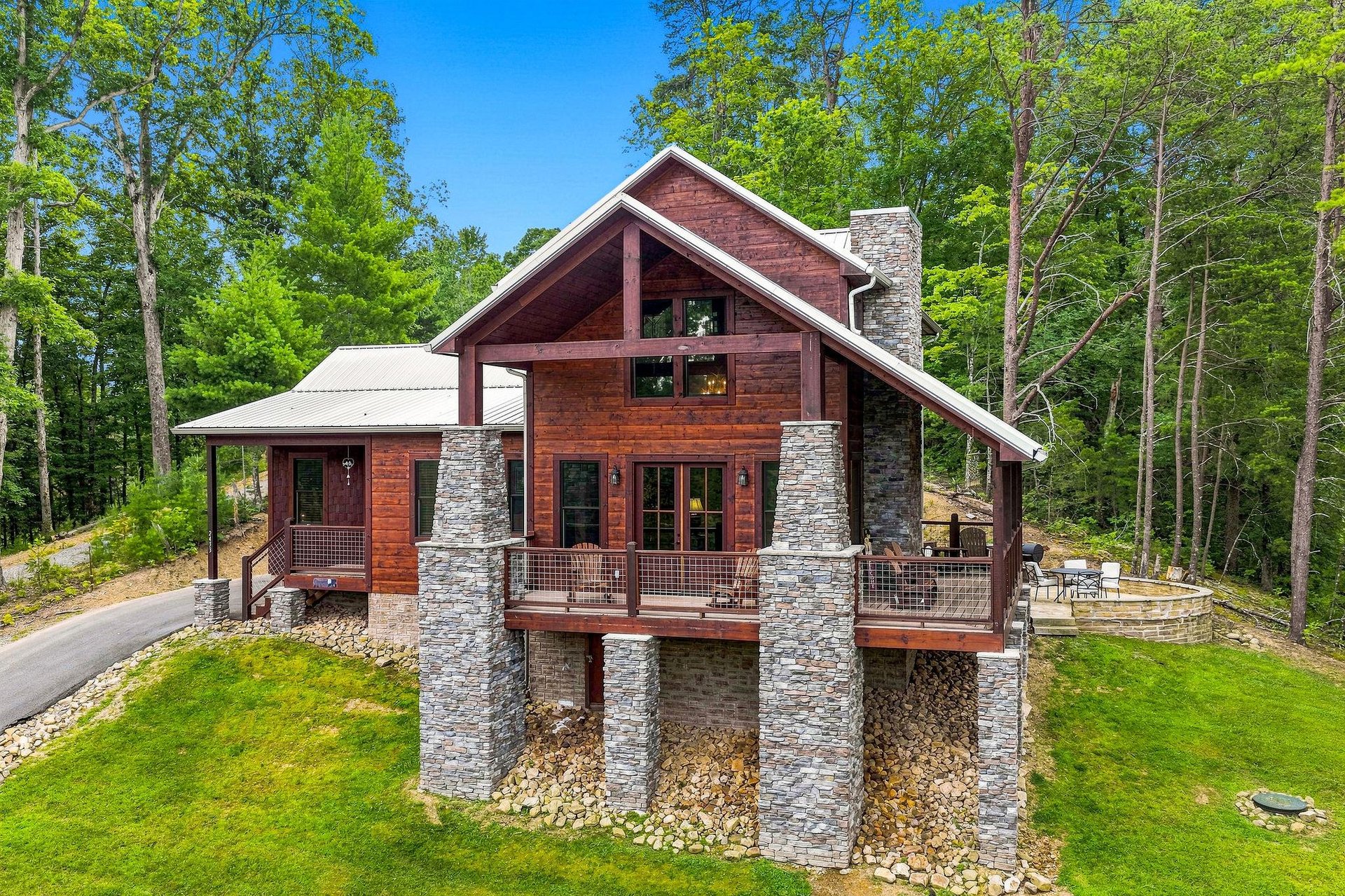 A stunning vacation home with rustic wood siding and stone accents nestled in a lush forest. The property features expansive decks and charming architectural details, surrounded by vibrant greenery an
