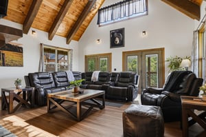 Sink into plush leather recliners and unwind beneath soaring vaulted wood ceilings. Natural light floods this open living room, where windows frame lush greenery and invite mountain breezes inside.
