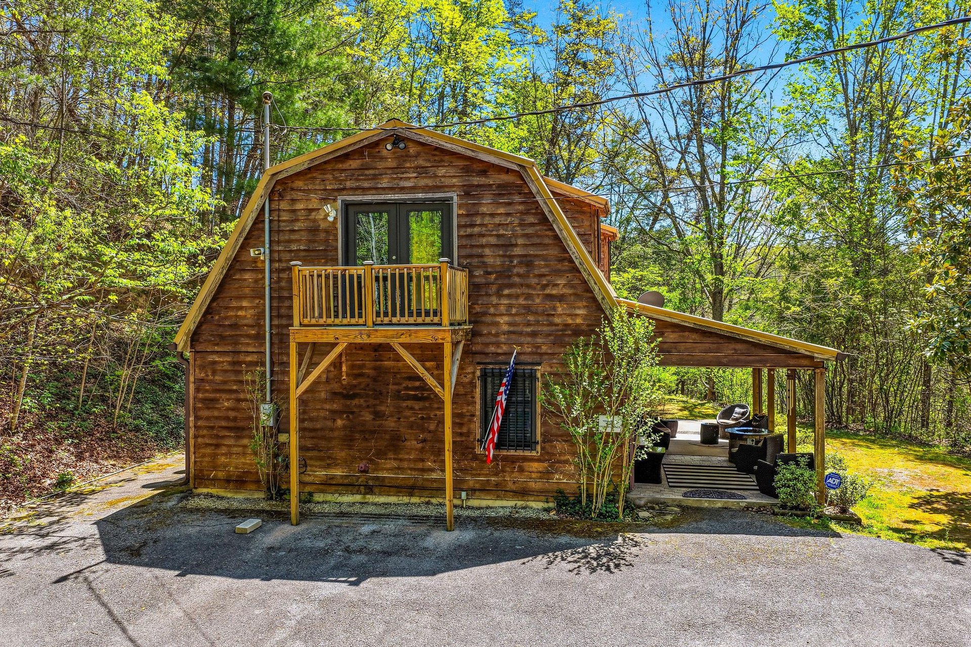 Charming rustic cabin nestled among lush spring foliage with a welcoming balcony and covered parking area.
