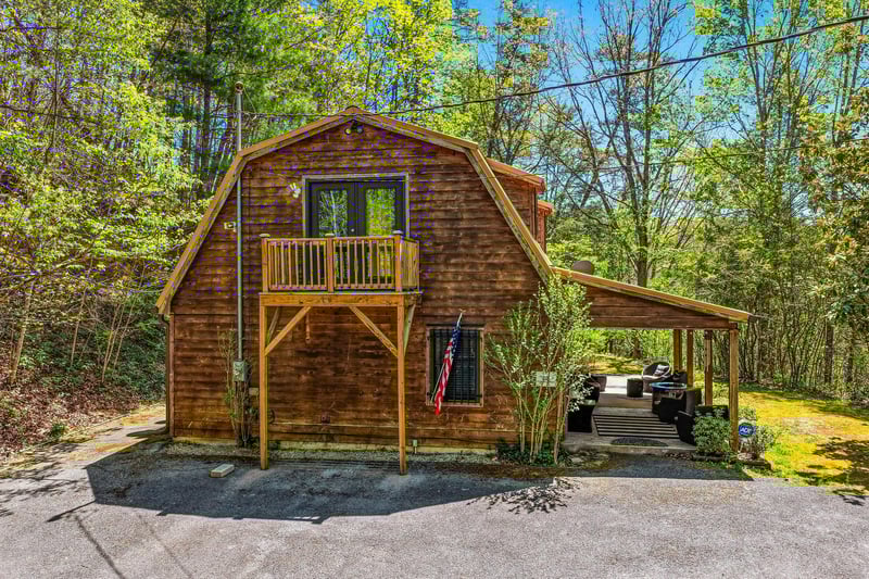 Charming rustic cabin nestled among lush spring foliage with a welcoming balcony and covered parking area.