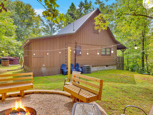 Charming woodland cabin surrounded by lush forest, featuring a cozy fire pit area with curved wooden benches for memorable evenings under the stars.