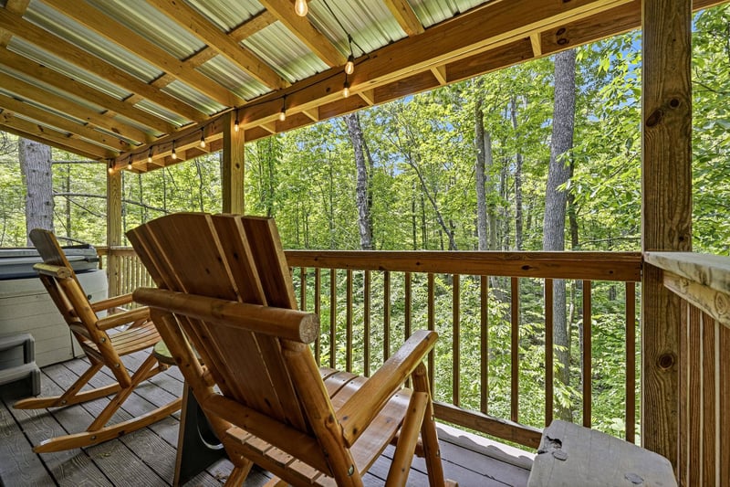 Settle into your private deck and let the forest embrace you. The rustic wooden chairs invite quiet moments while tall trees frame peaceful woodland views just beyond the railing.