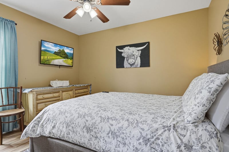 Drift off in this peaceful bedroom, with soft linens, a ceiling fan above, and charming artwork creating a welcoming retreat just for you.