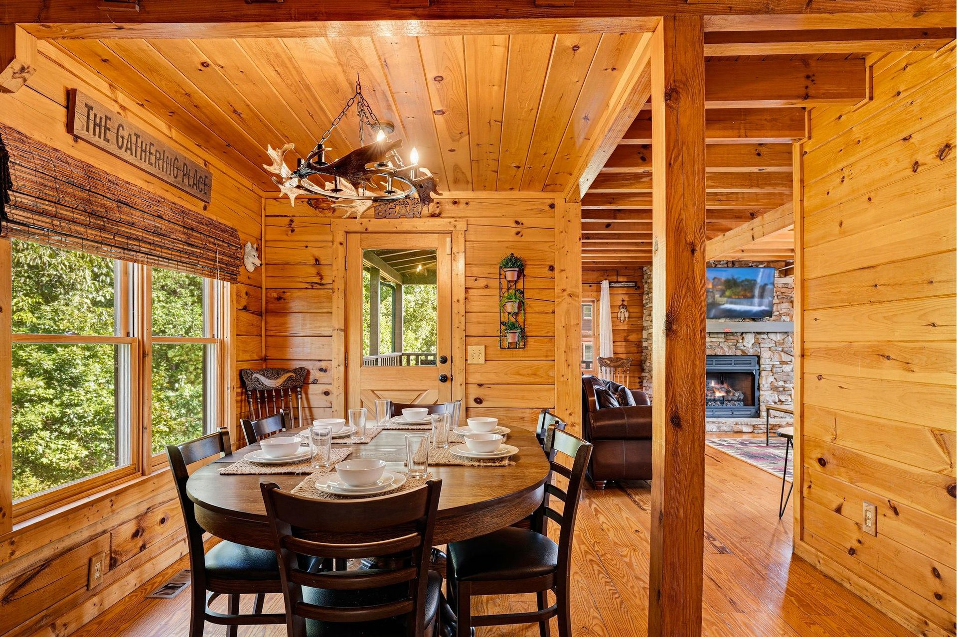 Gather around the rustic wood dining table beneath the charming chandelier, where warm pine walls and green views through the windows create the perfect cabin retreat for your shared meals.