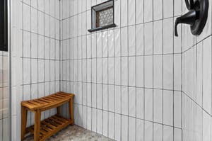 Walk in shower with tile walls and wooden bench