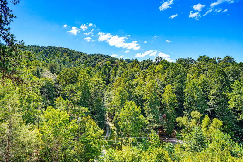 The property is nestled in a peaceful natural setting with lush forested hills and distant mountain ridges, offering a serene backdrop for your mountain getaway.