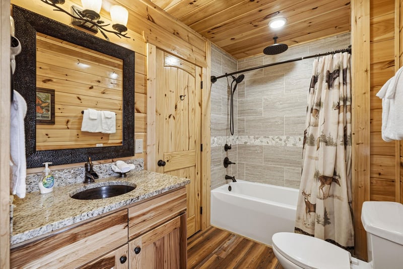 Unwind in your rustic bathroom featuring warm wood walls, granite counters, and a relaxing tubshower combo.