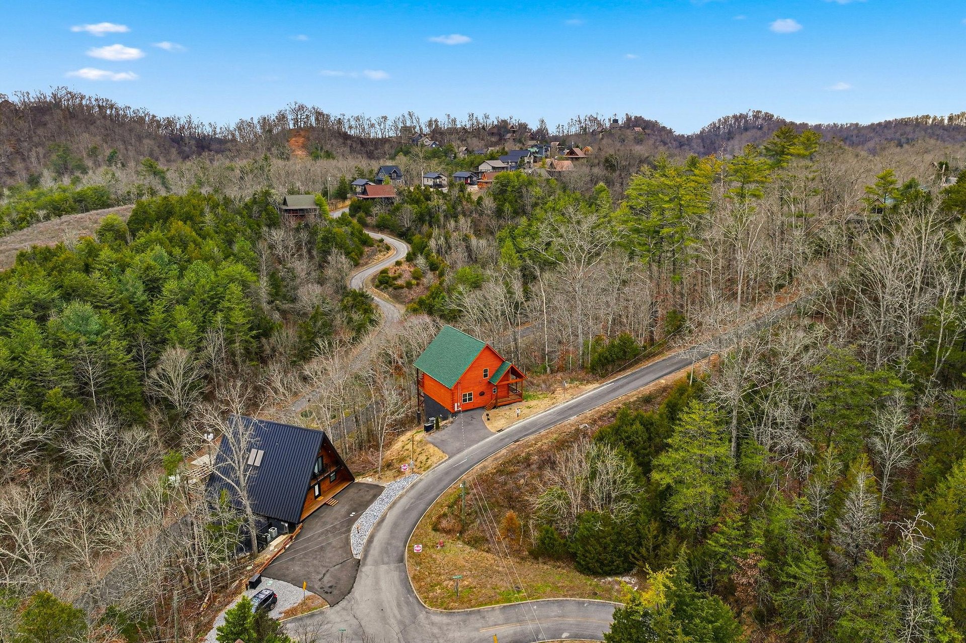 Aerial view of vacation cabins nestled among rolling forested hills, connected by winding mountain roads.