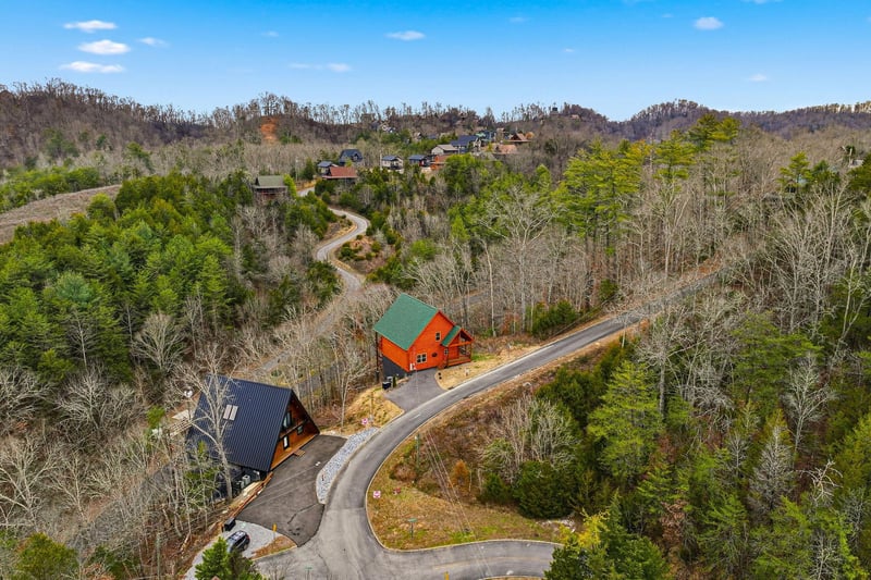 Aerial view of vacation cabins nestled among rolling forested hills, connected by winding mountain roads.