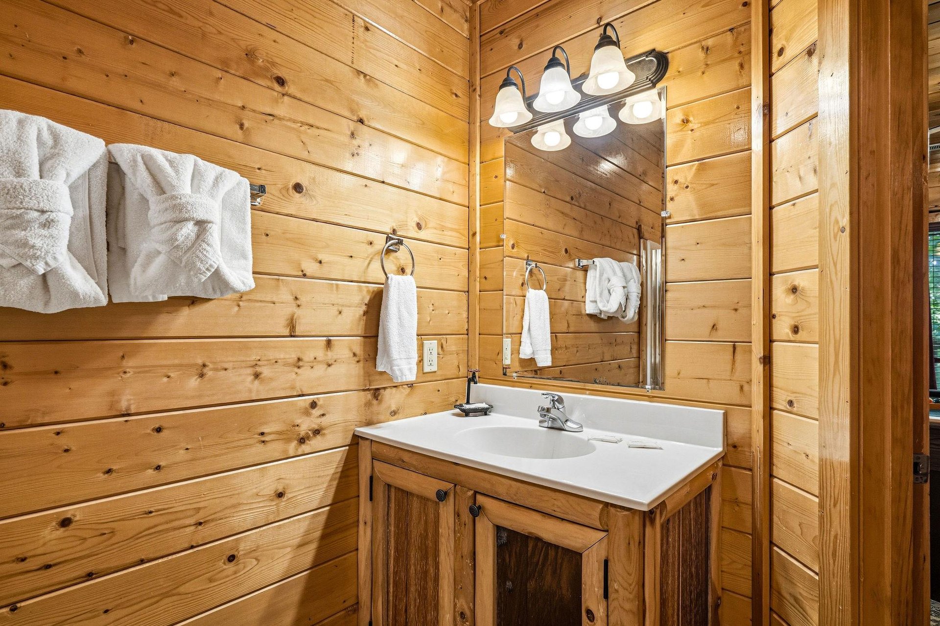 Your rustic bathroom features warm pine walls, fresh white towels, and charming vanity lighting—creating a cozy, cabinstyle retreat perfect for unwinding.