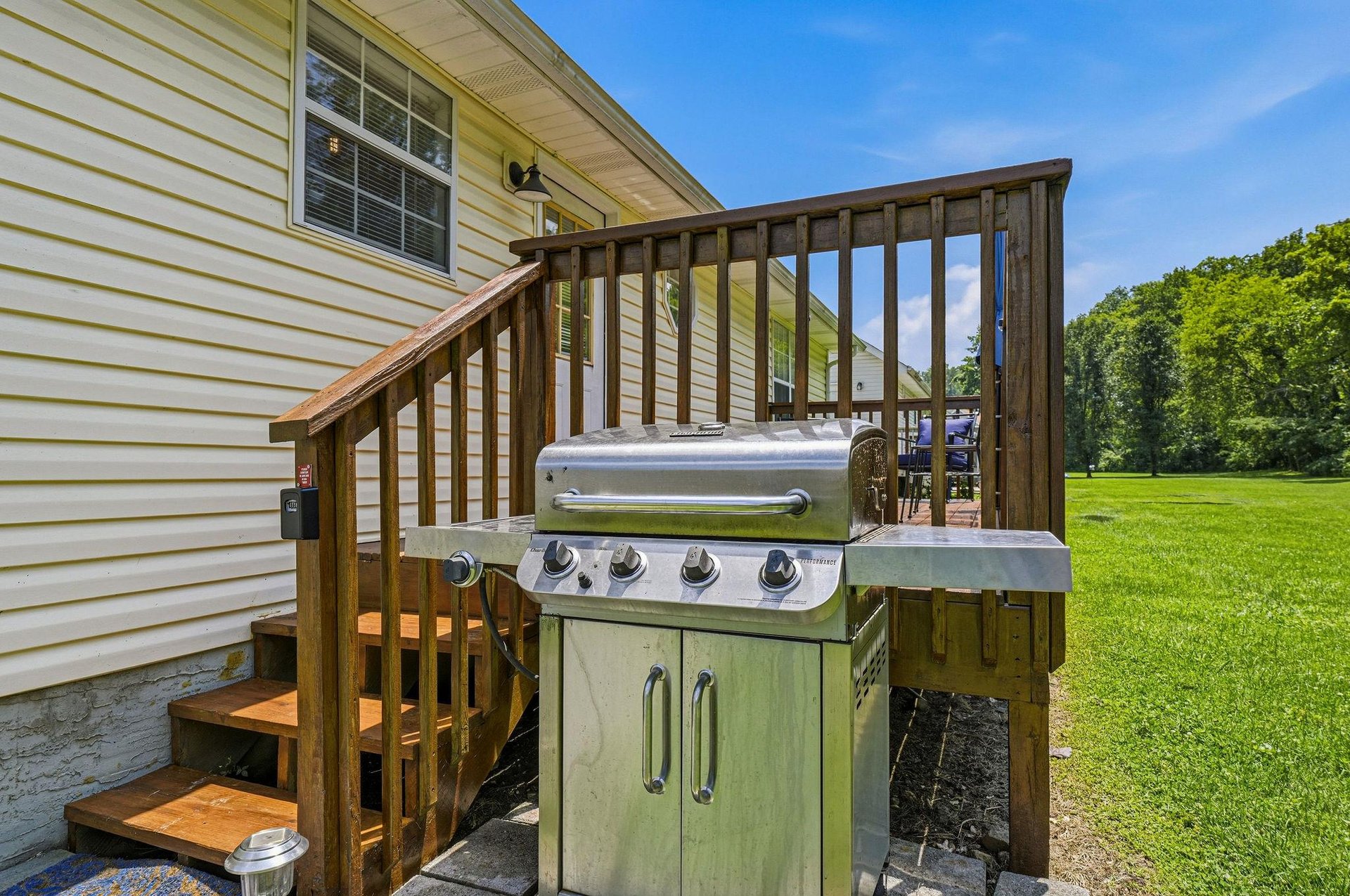 The property features an outdoor BBQ grill setup on the deck, perfect for enjoying a cookout surrounded by lush green lawns and open space.
