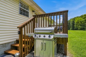 The property features an outdoor BBQ grill setup on the deck, perfect for enjoying a cookout surrounded by lush green lawns and open space.