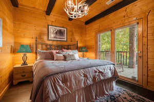 Sink into plush bedding beneath a striking antler chandelier, with your private balcony just steps away—wake to forest views and fresh mountain air.