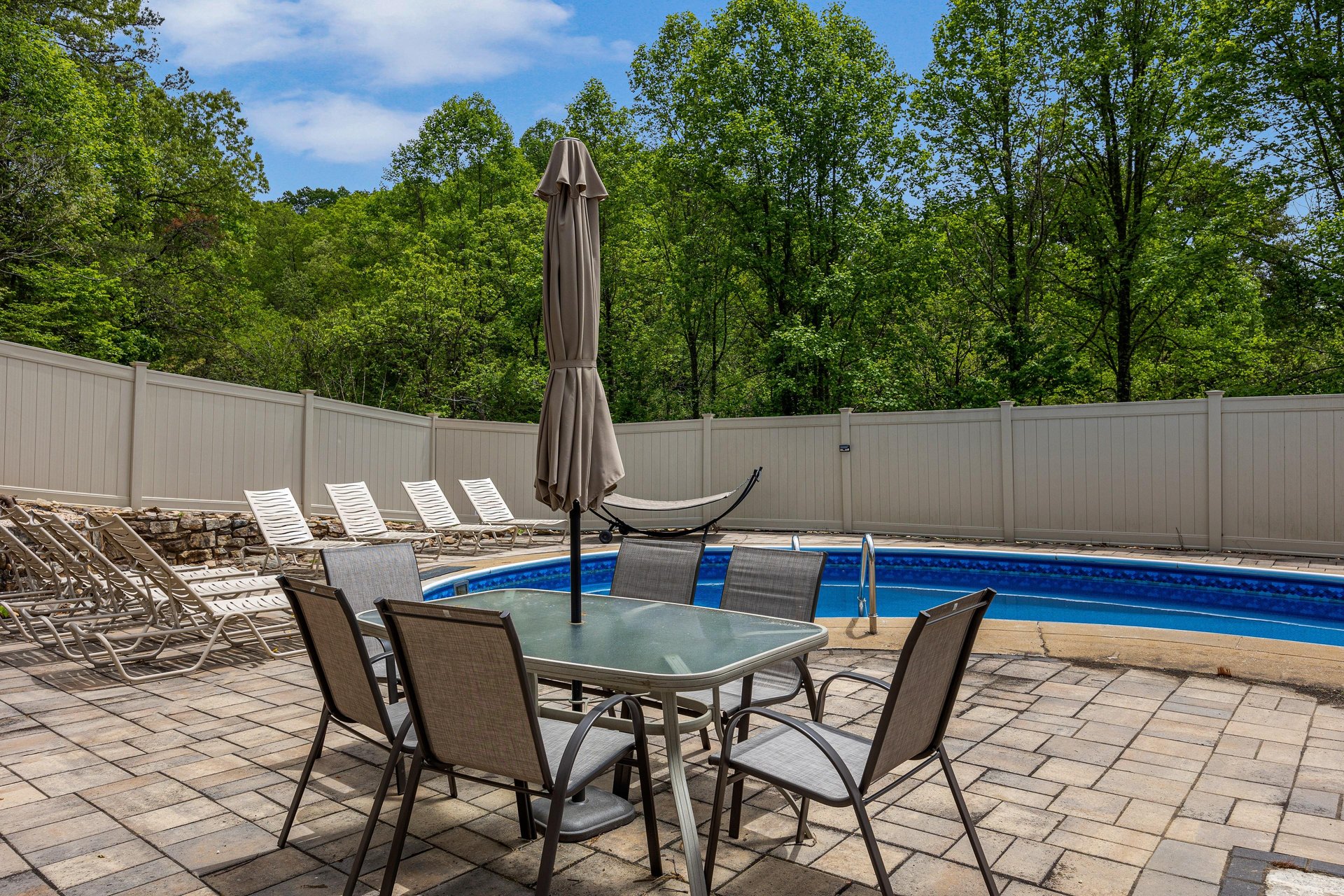 A peaceful pool area surrounded by lush greenery, with sunny lounge chairs and shaded outdoor dining, perfect for warm days.