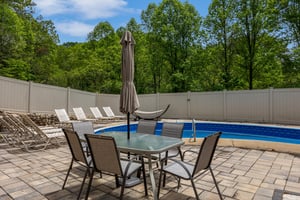 A peaceful pool area surrounded by lush greenery, with sunny lounge chairs and shaded outdoor dining, perfect for warm days.